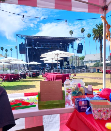 A carnival prize table set up in front of a large concert stage at an outdoor festival produced by Zebra Entertainment.